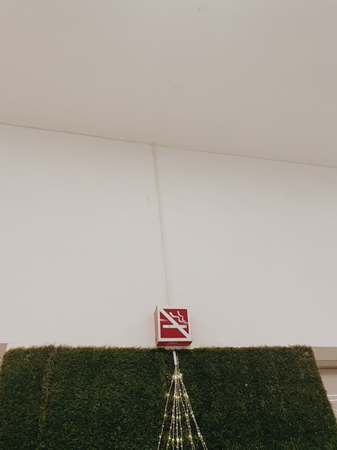 A no-smoking sign is mounted above a section of wall covered in artificial green grass. There are decorative lights arranged in a triangular pattern hanging down from the sign.