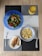 A meal is arranged on a textured placemat with geometric patterns. A vibrant blue bowl contains a fresh salad with leafy greens, diced tomatoes, cucumbers, and avocado. Next to it is a bowl filled with cooked grains, likely quinoa or bulgur, in a white and blue-rimmed bowl. A plate features grilled chicken breast with grill marks, placed beside a fork. A decorative glass holds an orange beverage, possibly juice.