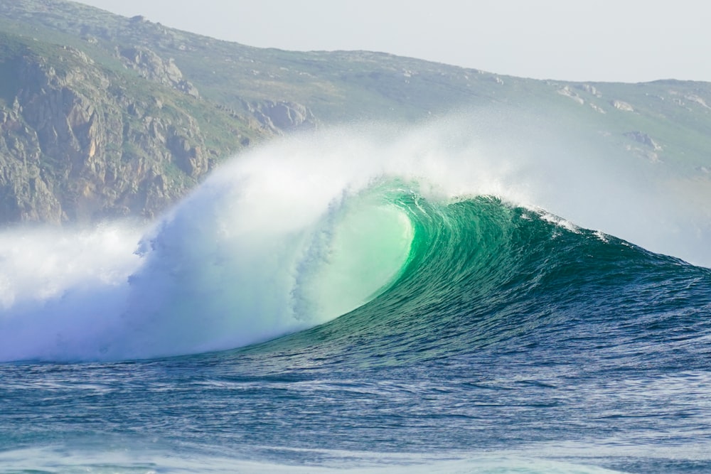 a large wave is breaking in front of a mountain