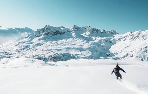 A skier on a wide snowy slope with mountain peaks behind
