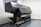 A large industrial printer is positioned in a clean, white-walled room. The printer is branded with the name Epson and appears to be printing or set up for a print job, with a green patterned material partially rolled through it. The room has a minimalistic look, with visible floor and wall fixtures.