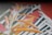 A close-up view of an abstract artwork on canvas featuring elongated orange and white forms interspersed with green and striped black and white elements. The composition includes dynamic brush strokes with vibrant colors, giving a sense of movement and complexity.