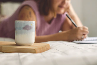 a woman writing on a notepad next to a coffee mug