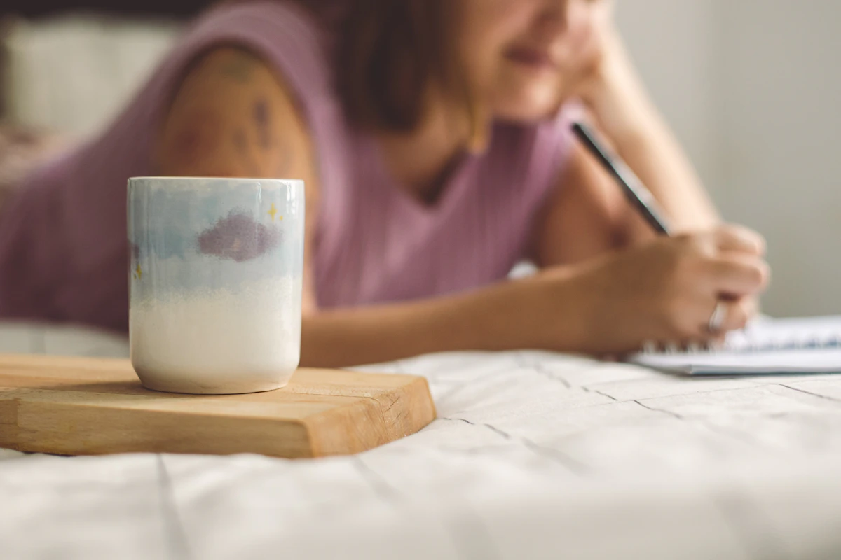 A woman writing in a notepad at a table next to a cup of coffee