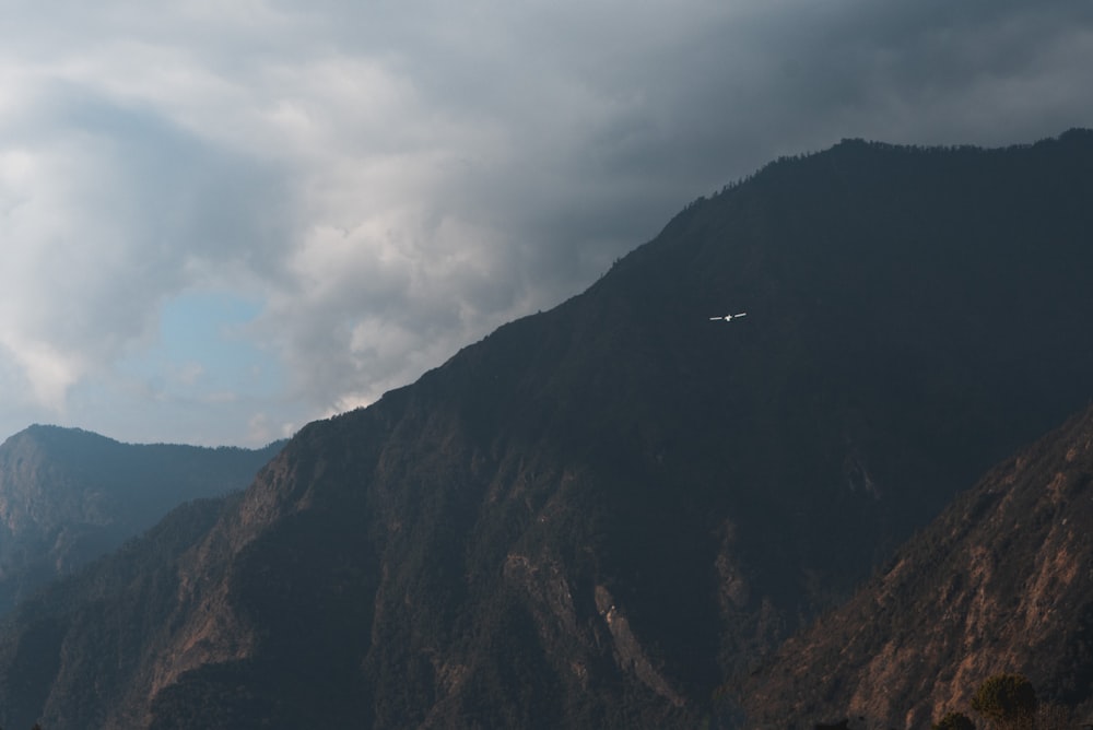 a plane flying over a mountain range under a cloudy sky