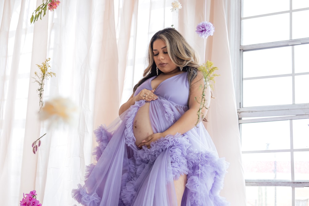 窓の前に立つ紫色のドレスを着た妊婦