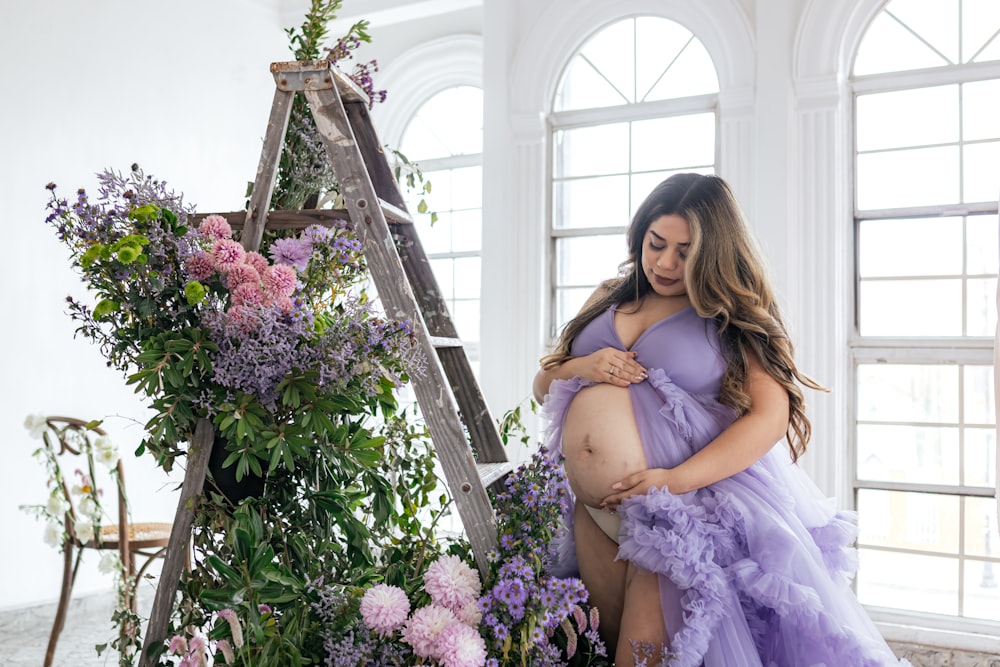uma mulher grávida em um vestido roxo de pé ao lado de uma escada