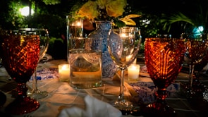 An elegant table set outdoors with fine china, candles, and fresh flowers under a twilight sky.