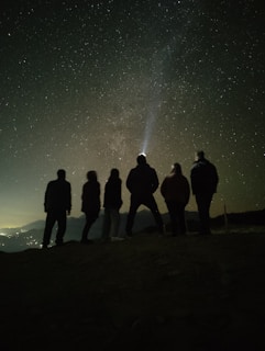 a group of people standing on top of a hill under a night sky