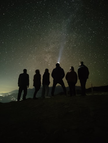 a group of people standing on top of a hill under a night sky