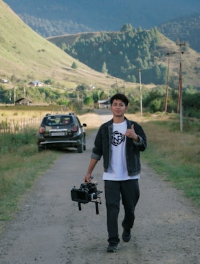 a man walking down a dirt road holding a camera