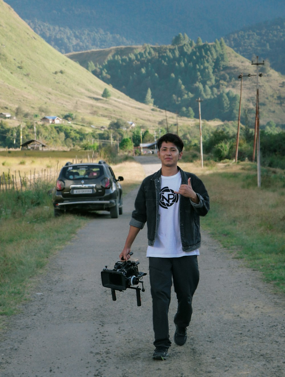 a man walking down a dirt road holding a camera
