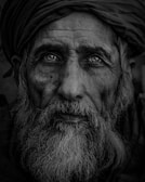 Portrait of an elderly man with deep lines and expressive eyes, wrapped in a traditional shawl.
