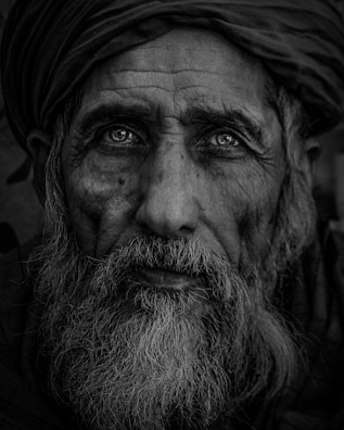 Portrait of an elderly man with deep lines and expressive eyes, wrapped in a traditional shawl.