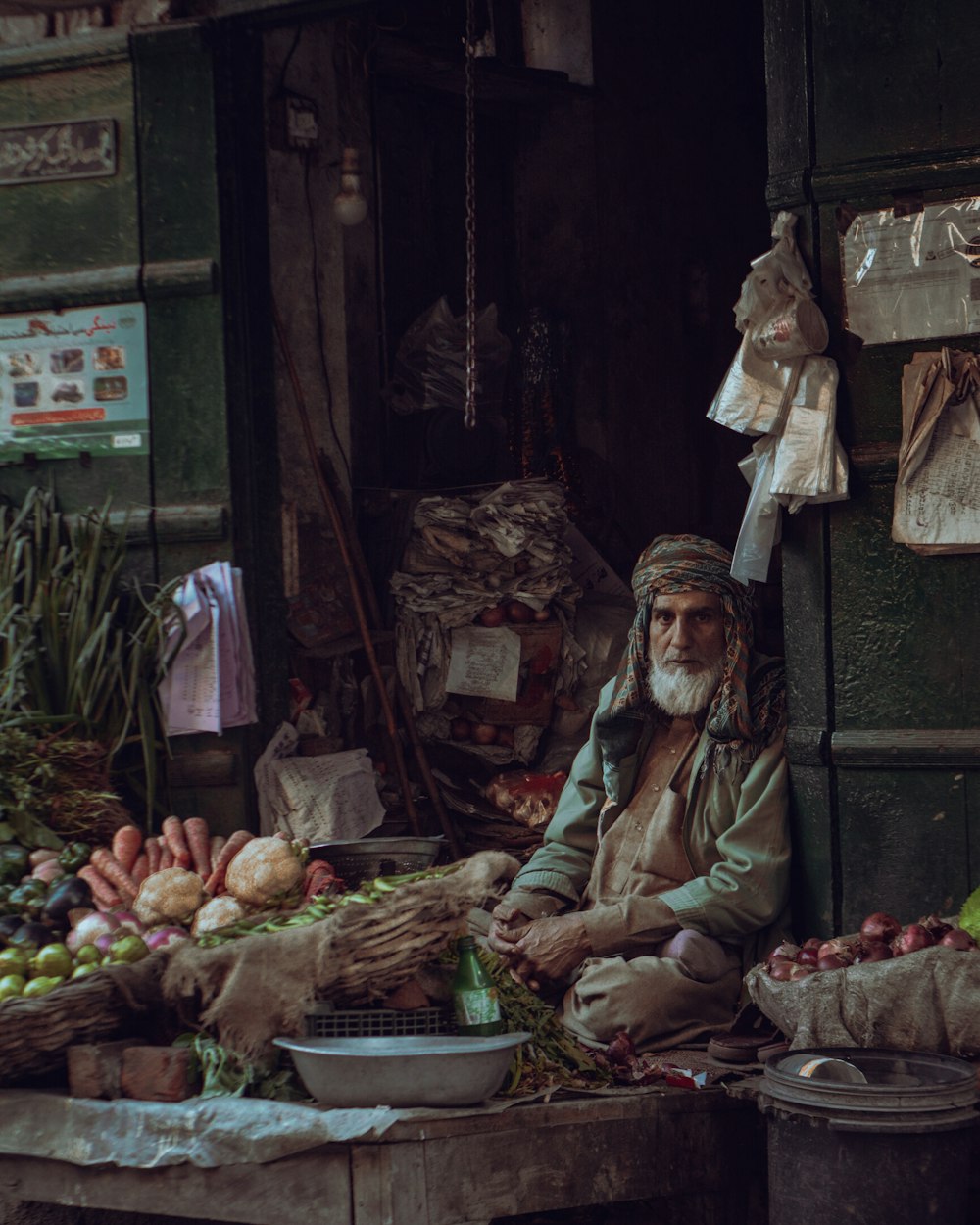 a man sitting in front of a fruit and vegetable stand