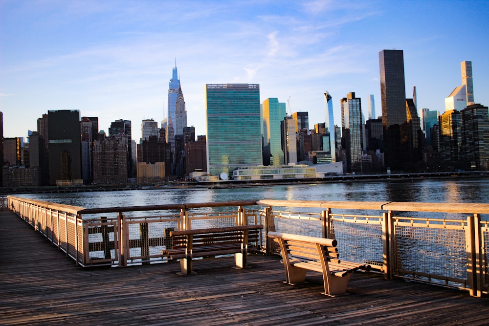 a wooden pier with benches overlooking a city skyline