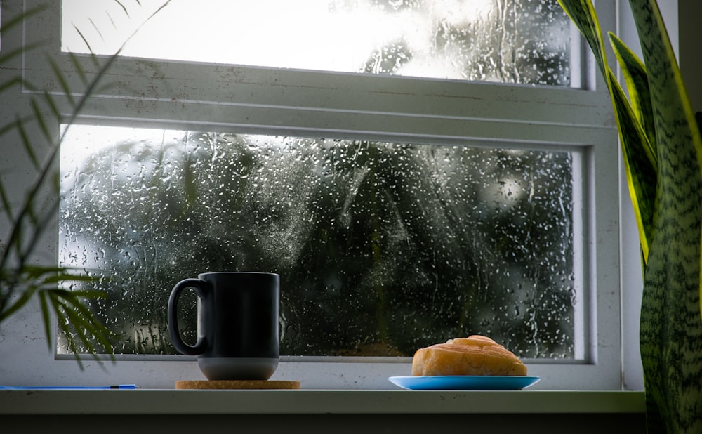 a cup of coffee and a piece of bread on a window sill