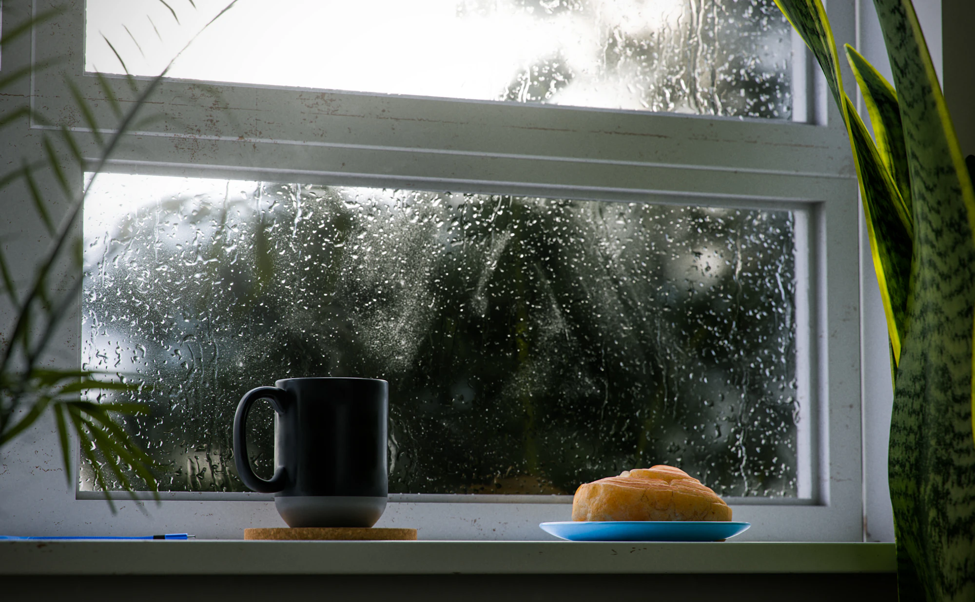 A cup of coffee on a windowsill with heavy rain running down the glass outside