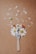 A paintbrush is adorned with fresh daisies and a few small red flowers. Petals are scattered around, creating a dynamic and artistic composition on a brown textured background.