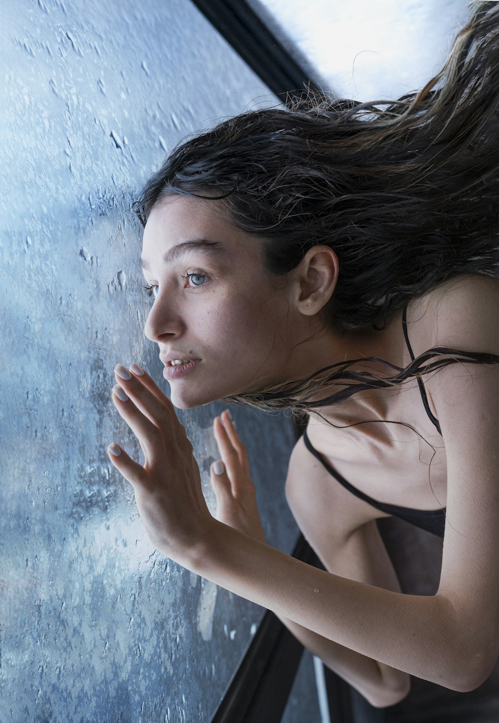 a woman standing in front of a window with her hair blowing in the wind