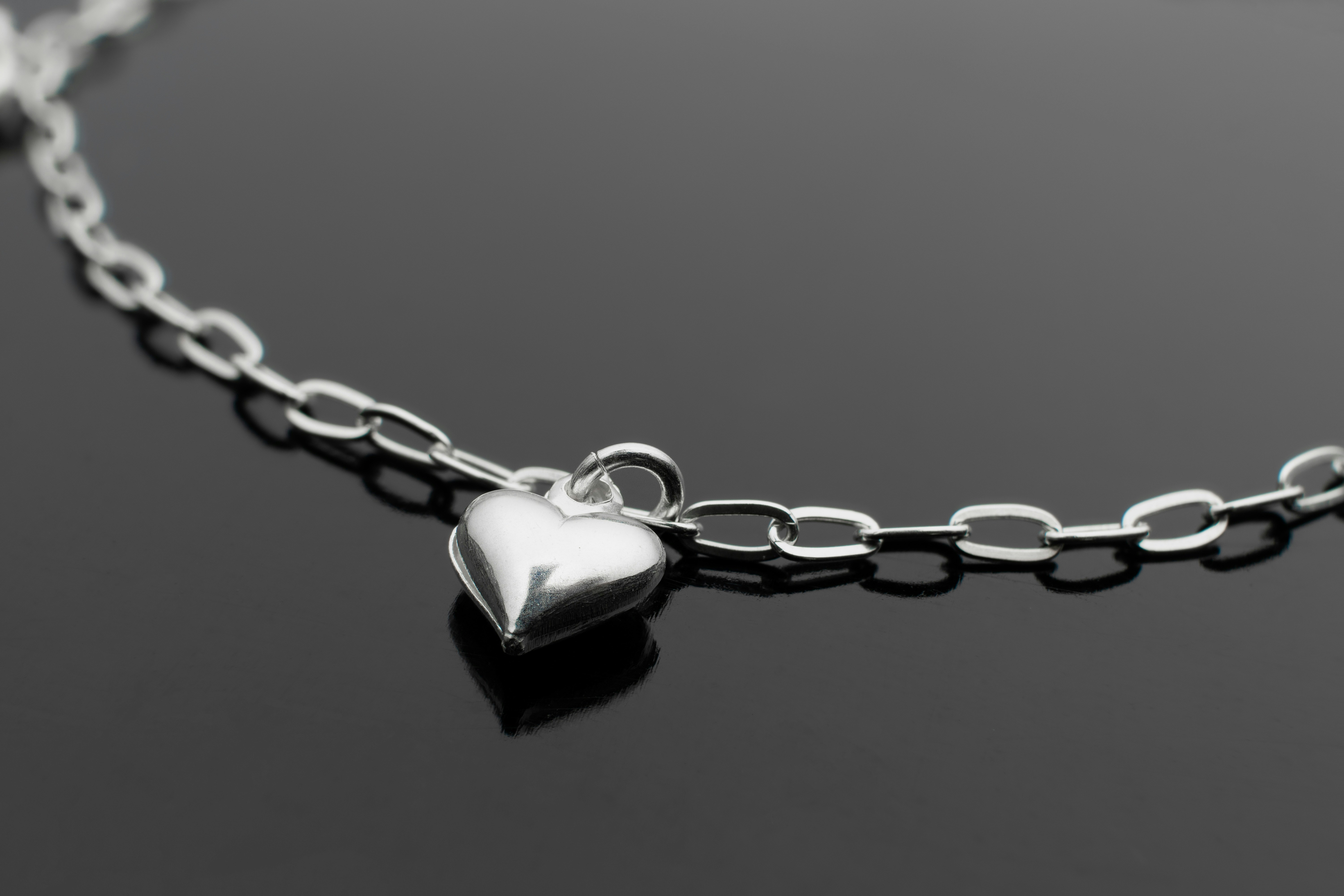 Beautiful silver necklace heart shaped pendant on a dark reflective surface as background