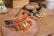 Intricately designed bracelets featuring vibrant colors and dangling ornaments rest on a textured wooden surface. One bracelet is woven with orange thread, showcasing gold charms and colorful beads, while the other has a black base with similar gold details.