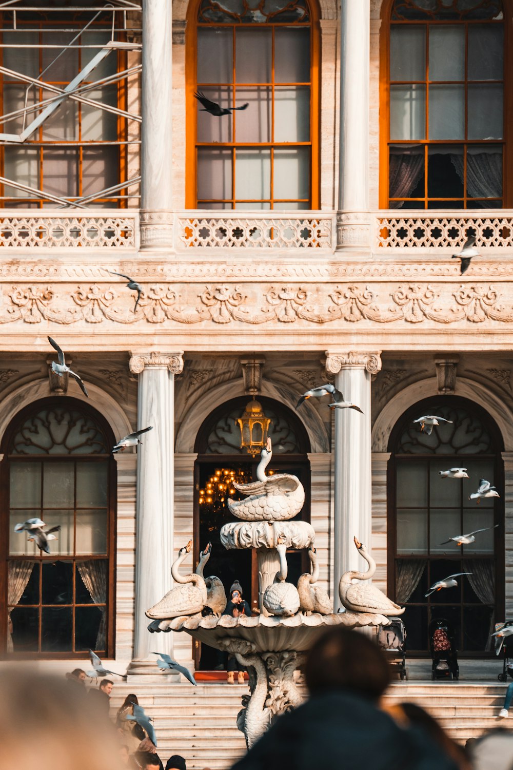 a flock of birds flying over a fountain in front of a building