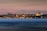 A panoramic view of Istanbul's skyline at dusk, featuring the illuminated silhouettes of historical landmarks against a soft pink and blue sky. The city lights reflect softly on the water in the foreground, adding a sense of calm and beauty.