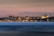 A panoramic view of Istanbul's skyline at dusk, featuring the illuminated silhouettes of historical landmarks against a soft pink and blue sky. The city lights reflect softly on the water in the foreground, adding a sense of calm and beauty.