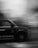 A black and white photo of a moving taxi captured in motion blur, highlighting the dynamic speed. The taxi is partially visible with text on its side, including a logo and social media handle.