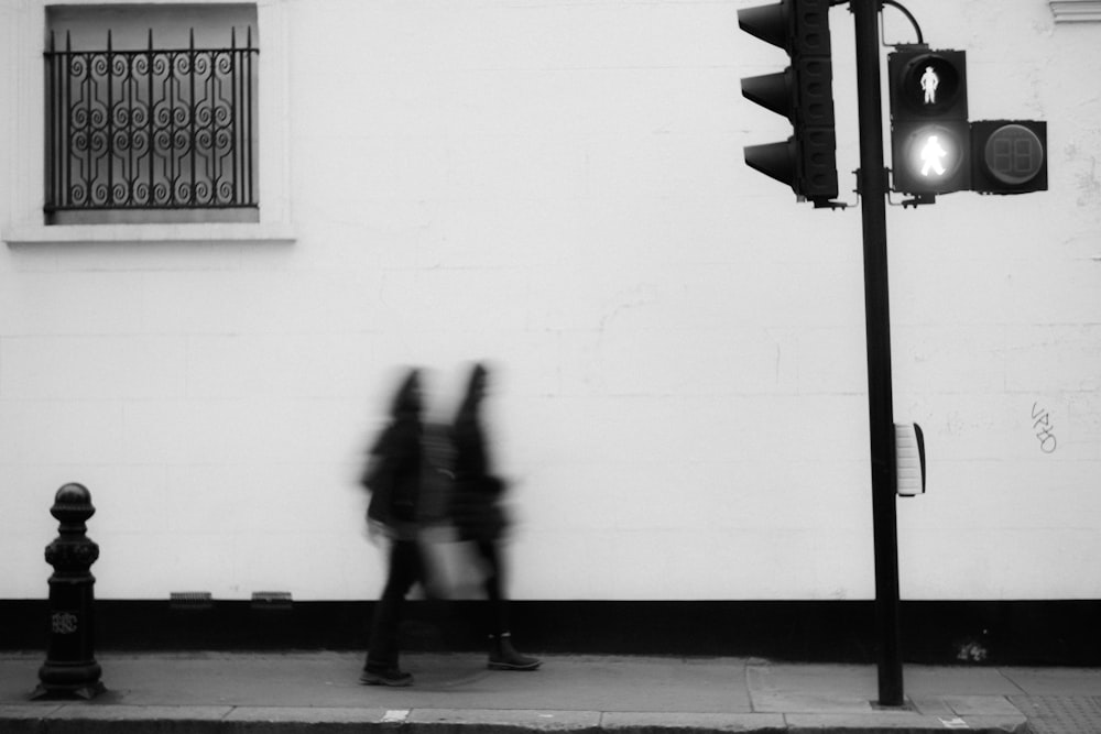 a black and white photo of a person walking past a traffic light