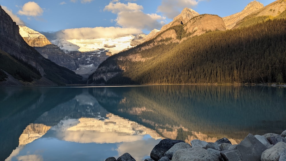 a lake surrounded by mountains under a cloudy sky