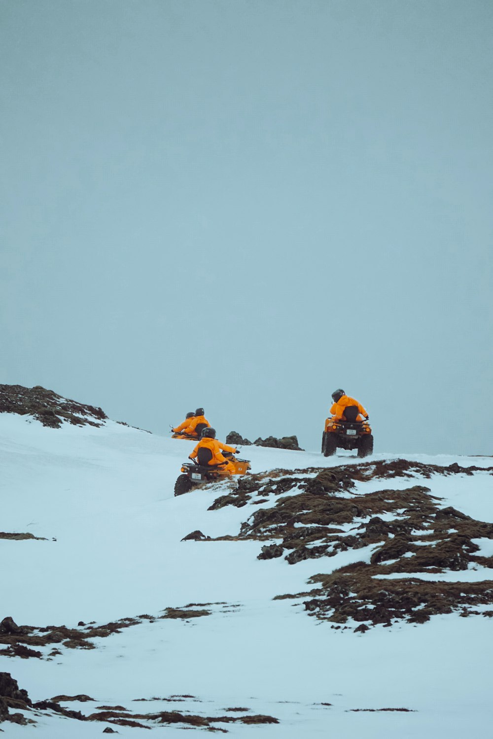 three people riding atvs on a snowy mountain