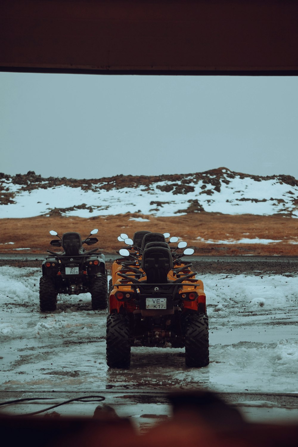 a couple of four wheelers driving down a snow covered road