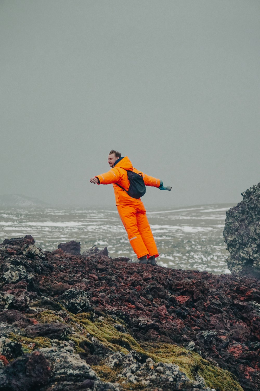 a man in an orange jumpsuit on a rocky beach