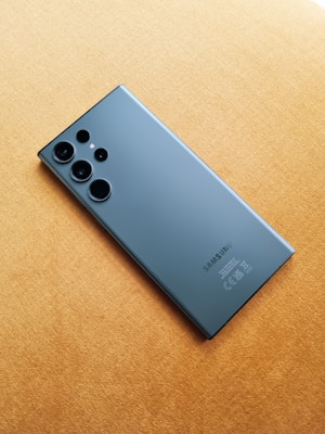 A sleek, modern smartphone with a black finish is placed on a soft, light brown surface. The phone features multiple camera lenses on its back panel, highlighting its advanced photography capabilities.