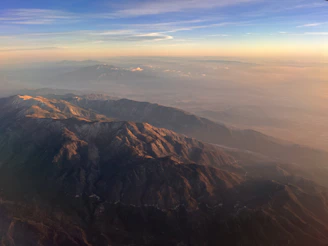 A panoramic view of a mountain range at sunset, with deep shadows and warm golden hues.