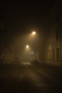A foggy Memphis street at night with dim lantern light casting eerie shadows on historic buildings.