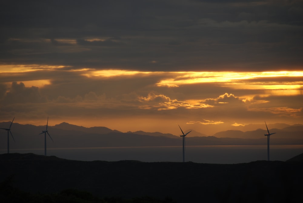 Un grupo de molinos de viento en una colina con una puesta de sol al fondo