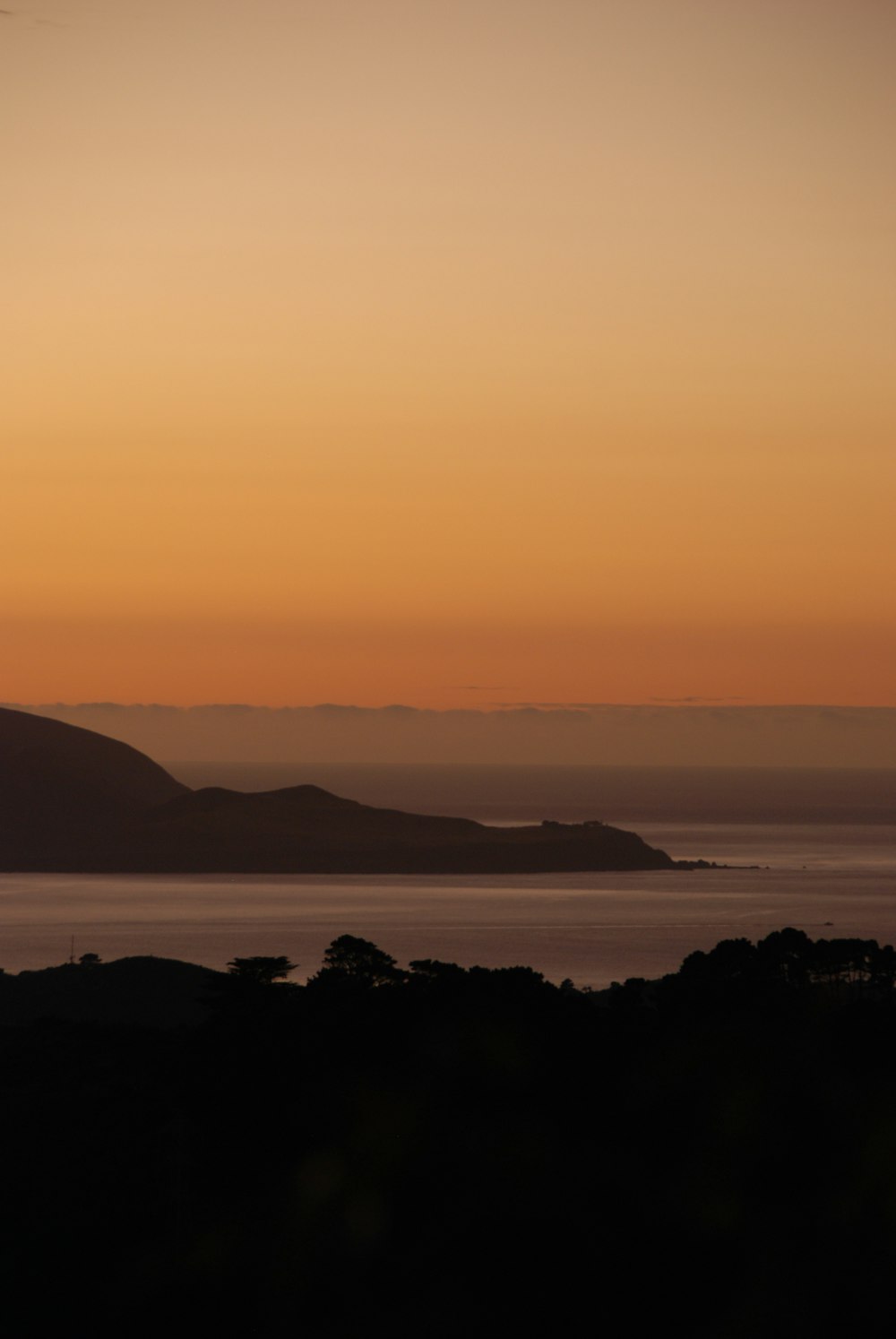 the sun is setting over the water and hills