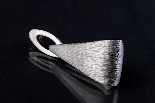 Close-up of a sleek black pendant resting on smooth white marble, highlighting its sharp edges and subtle shine.