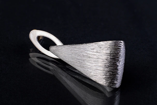 An elegant silver bullion pendant displayed on a simple black velvet cushion.