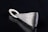 A sleek, silver metallic pendant with a textured surface lying on a black reflective surface. The pendant has an elongated triangular shape with a looped holder at one end.