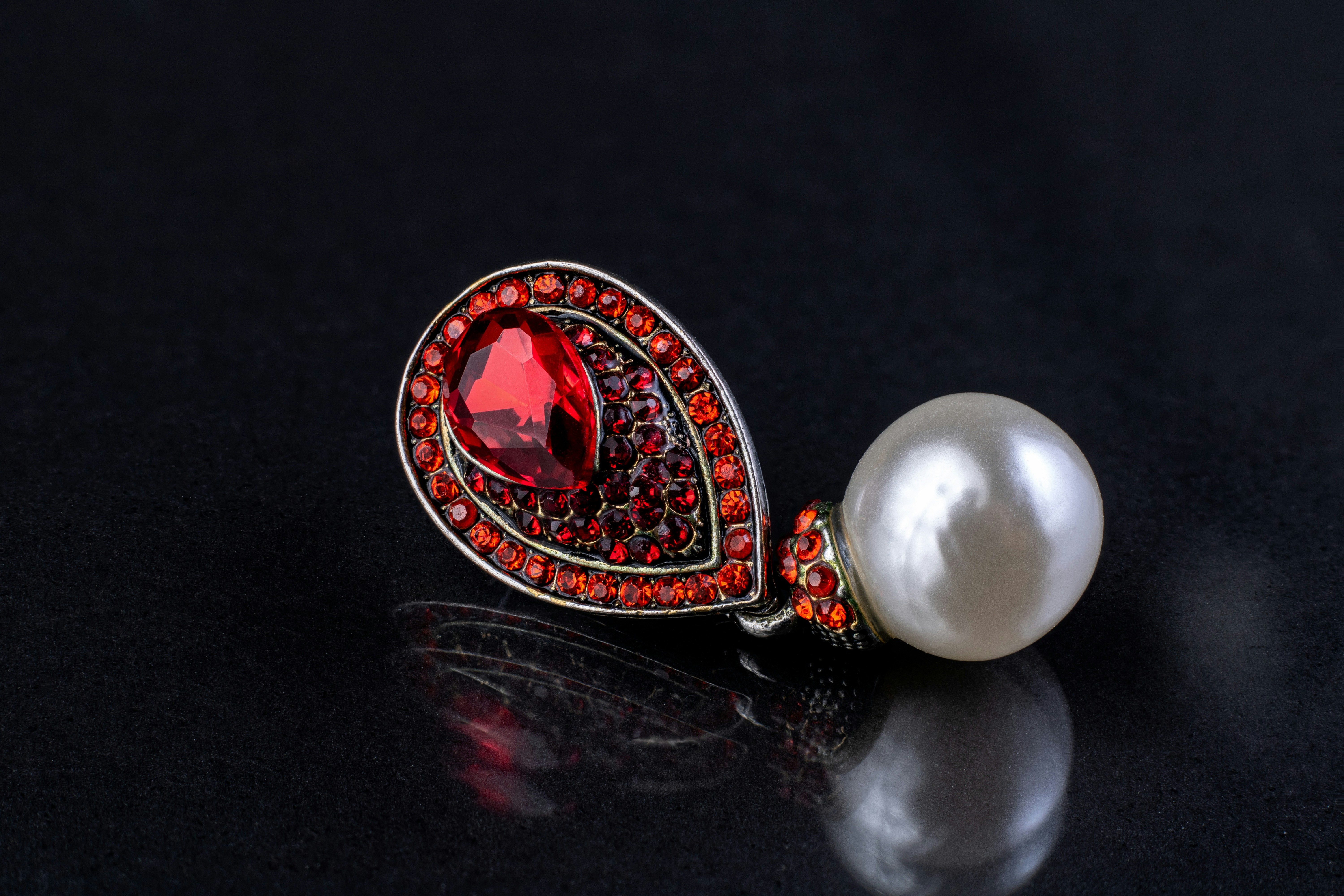 Beautiful earring with red gemstones on dark reflective surface as background
