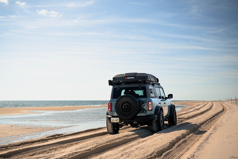 a jeep driving down a sandy road next to the ocean