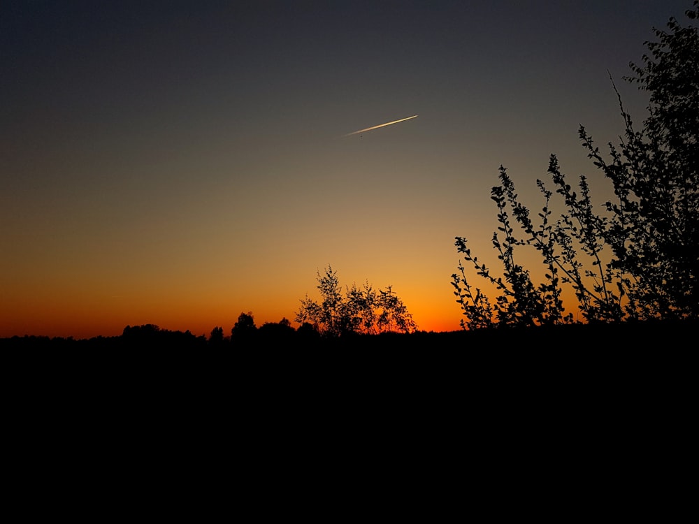 a sunset with a plane flying in the sky