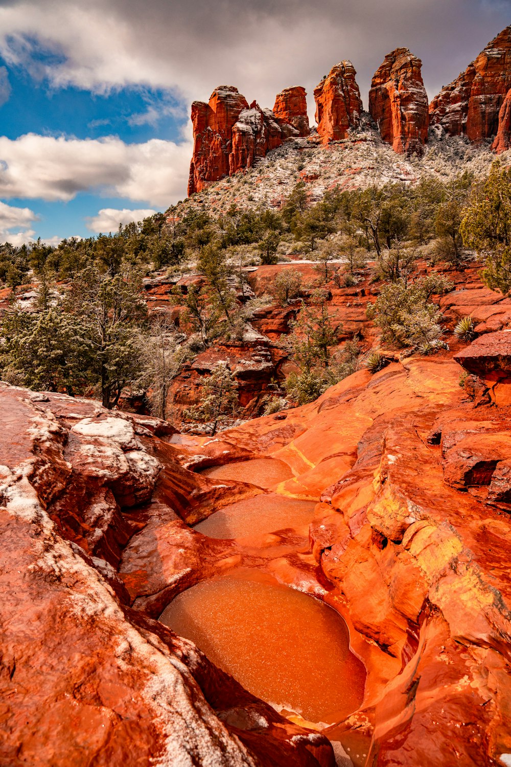 a red rock formation with trees and clouds in the background