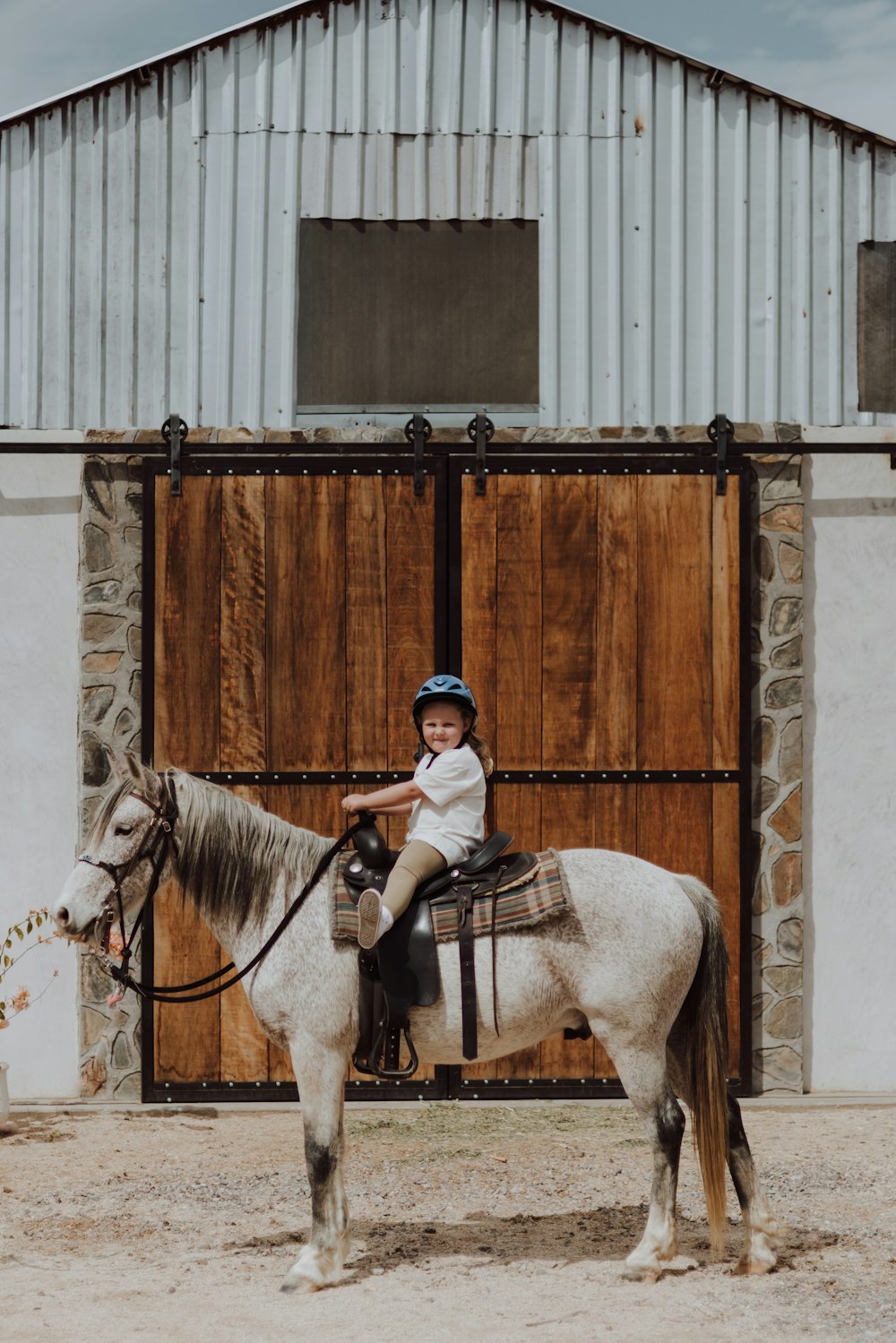 a young child riding a horse in front of a barn