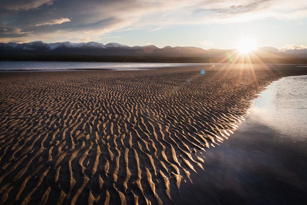 the sun is setting over a sandy beach