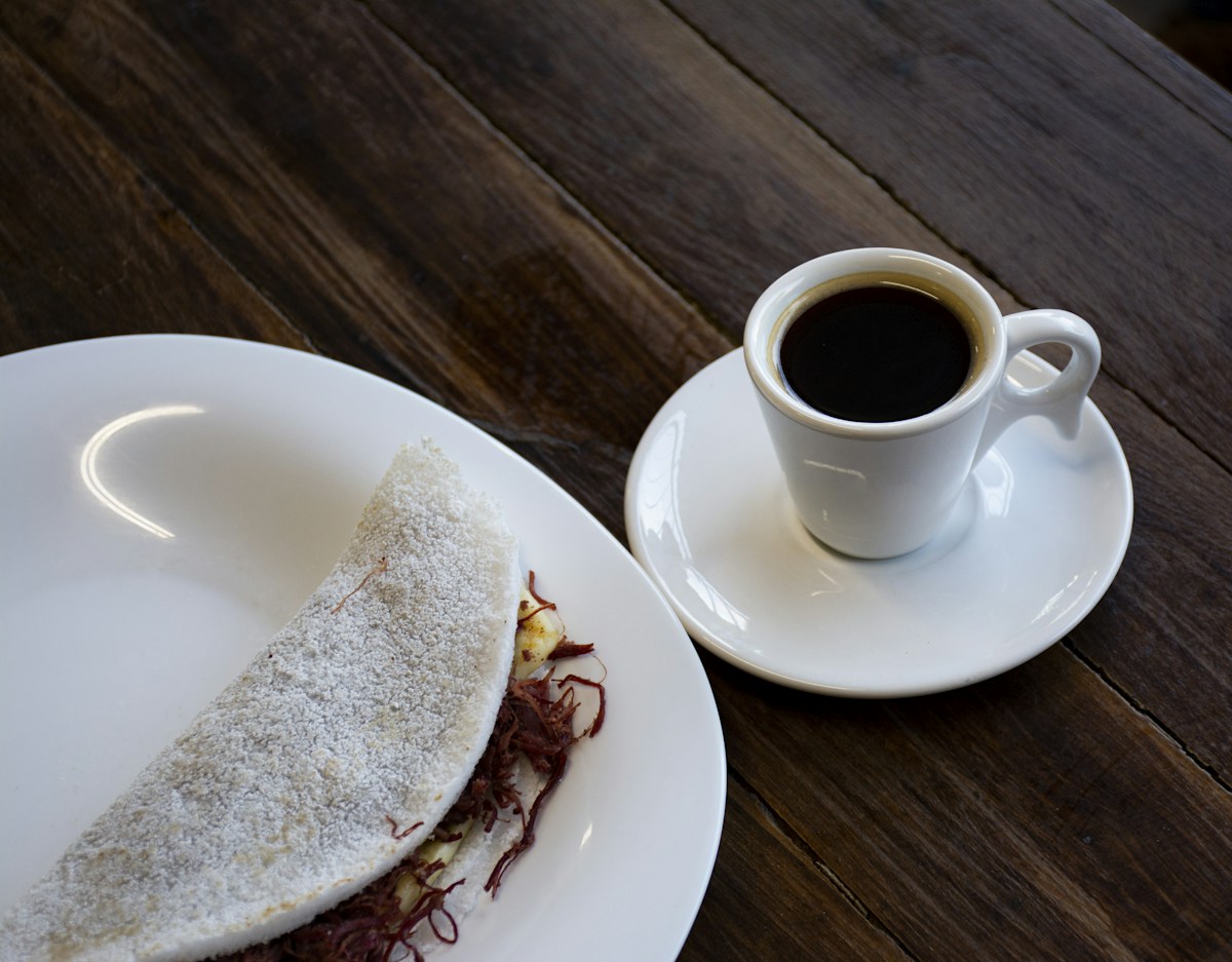 Tapioca recheada no prato ao lado de uma xícara de café
